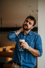 Wall Mural - Caucasian handsome man in a denim shirt having a beer and stretching his neck during an active pause.