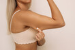 © Марина Демешко - Cropped shot of a young blonde woman grabbing skin on her upper arm with excess fat isolated on a light beige background. Pinching the loose and saggy muscles. Overweight concept
