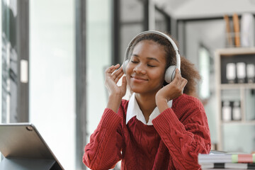 Wall Mural - Smiling African American Hispanic student looking up from laptop at campus library, using tablet and headphone, listen to music