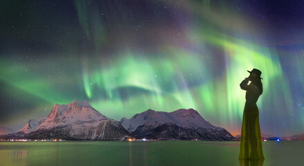 Wall Mural - young girl in dress and black hat walking on the water - northern lights (aurora borealis) in the sk