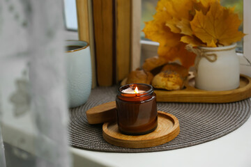 Poster - Burning aromatic candle near cup with hot drink, books, cookies and leaves on wicker mat. Autumn coziness