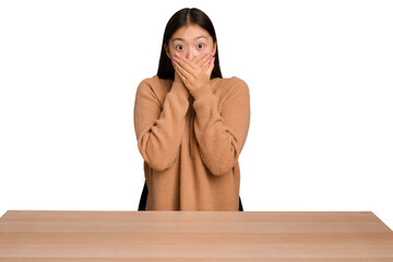 Wall Mural - Young asian woman sitting on a table isolated shocked covering mouth with hands.