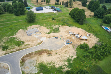 Two new houses being constructed on a cul-de-sac by a home builder. The one is a poured basement, and the other is already framed and has a roof.