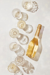 Flat lay with white sparkling wine bottle, set glasses wine with sunshine shadow and flare on light beige background. White wine aesthetic photo, copyspace. Summer holiday monochrome still life