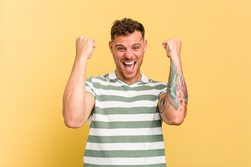 Young caucasian handsome man isolated on yellow background celebrating a victory, passion and enthusiasm, happy expression.