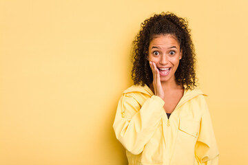 Wall Mural - Young Brazilian curly hair cute woman isolated on yellow background shouts loud, keeps eyes opened and hands tense.