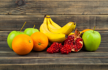 Poster - Oranges, apples, pomegranate and bananas on a wooden table.