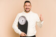 © Asier - Adult latin man holding a weight scale isolated smiling and raising thumb up