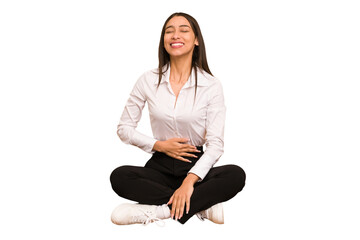 Young colombian woman sitting on the floor isolated touches tummy, smiles gently, eating and satisfaction concept.