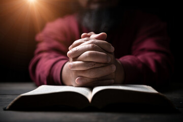 Wall Mural - Hands folded in prayer on a Holy Bible in church concept for faith, spirituality and religion, man praying in morning. Man hand with Bible praying. Person Christian who faith in Jesus worship in dark.