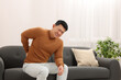 © New Africa - Asian man suffering from back pain on sofa indoors