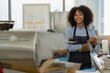 © ArLawKa - Smiling african american barista standing behind the coffee shop counter accepting customers, food and drink concept