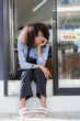 © ArLawKa - Young American woman sitting sad because there are no customers in front of the cafe door and food with open sign. She is a waitress at a restaurant preparing to open. to serve customers