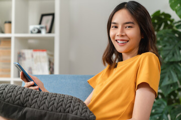 Wall Mural - Cheerful young woman holding a smartphone and using online social on lifestyle. Technology for communication concept.