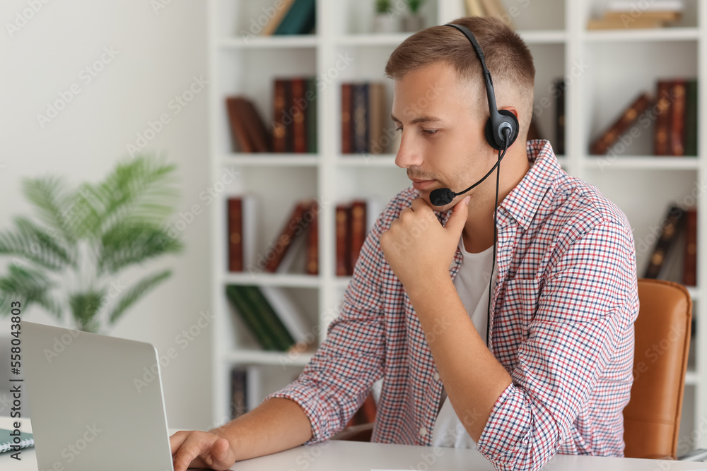 Young man with headset and laptop studying online at home