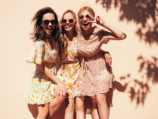 Three young beautiful smiling hipster female in trendy summer dress clothes. Sexy carefree women posing in the street. Positive models having fun outdoors at sunny day. Cheerful and happy. Near wall