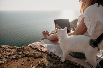 Woman sea laptop. Business woman petting cat and working on laptop by the sea. Close up on hands of pretty lady typing on computer outdoors summer day. Freelance, digital nomad and holidays concept.