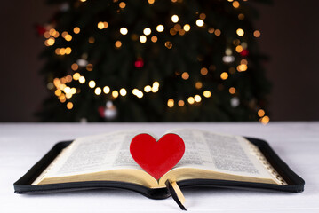 An open Bible on the table. The heart is a symbol of God's love for people. Prayer. On the background of the Christmas tree