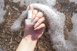 Female hand with beige nail design. Female hand with mate beige nail manicure hold beige nail polish bottle on sea waves
