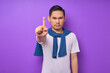 © Bangun Stock Photo - angry young Asian man wearing white t-shirt looking at camera and showing stop gesture with his index finger isolated over purple background. people lifestyle concept