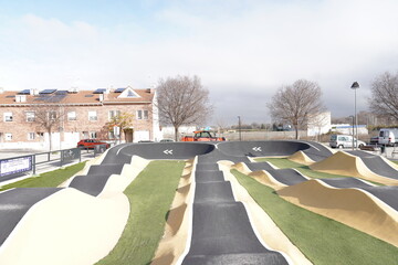 Pump track in black, yellow and with artificial grass; for wheeled vehicles such as bicycles, skates and scooters.