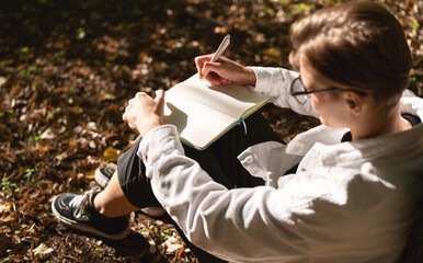 Short hair woman sitting in park on ground and writing notes in her diary.