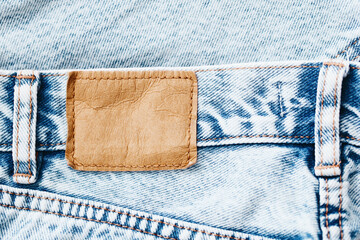 Wall Mural - Fashion background with empty copy space for graphic design. Blank leather label tag. Blue jeans denim texture with thread sew lines. Brown clothing tag.