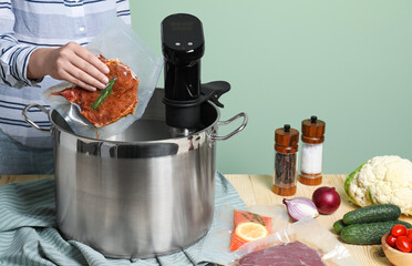 Wall Mural - Woman putting vacuum packed meat into pot with sous vide cooker at wooden table, closeup. Thermal immersion circulator
