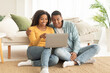 © Prostock-studio - Happy millennial african american husband hug wife, watch video on laptop, have online call, sit on floor