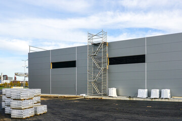 Canvas Print - Gray sandwich panel facade of a unfinished warehouse building, tubular multilevel scaffolding