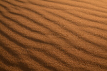 Incredible Wavy Diagonal Patterned Textured Sand Waves On A Desert Or Beach With Beautiful Golden Light Running Across Tiny Pebbles Specks Of Sand.