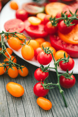 Delicious raw fresh cherry red and yellow tomatoes. Sliced colorful tomatoes on white round plate on wooden background. Healthy food rich in vitamin C