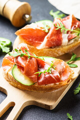 Sticker - Appetizer crostini, open sandwiches with cream cheese, prosciutto, cucumber and arugula at cutting board.