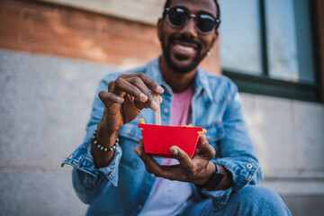 Close up shot of man pricking some french fries while he is sitting on the street