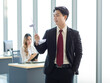 © Bangkok Click Studio - Millennial Asian young professional successful male businessman manager in formal suit standing smiling holding windmill model showing thumb up in company office while colleague working at workplace