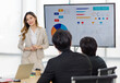 © Bangkok Click Studio - Asian professional successful female businesswoman lecturer presenter in formal suit standing smiling at graph chart data monitor answer questions to male colleague in company office meeting room