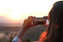 A Woman Uses Her Smartphone To Take Pictures Of The Sunrise In A Valley With Abundant Nature Tourism And Technology.