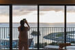 ホテルから見える、海に沈む夕日を撮影する女性