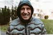 middle-aged man, in winter jacket with hood, smiles an ugly smile with crooked spoiled teeth 