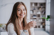Confident blonde businesswoman sitting at kitchen table home drinks water looks at camera against blurry interior. Successful Italian fit woman satisfied by healthy lifestyle. Wealth and health care.