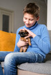 © lelechka - Boy playing with baby dog. Kid play with puppy at home. Little boy and griffon or brabanson dog on sofa. Children and pets at home. Kid sitting on the floor with pet. Animal care.