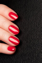 Wall Mural - Female hand with beautiful manicure - red nails on black leather surface background. Nail care concept