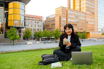 Wall Mural - Young asian woman in headphones writing down notes outdoors