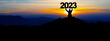 Happy new Year - Landscape background banner panorama 2023 - Breathtaking view with black silhouette of mountains and man holding year, in the morning during the sunrise
