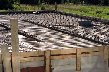 A steel reinforcement for the concrete floor and pillars on the first floor of a house under construction, a wooden formwork, a smoke and ventilation chimney, walls made of aac