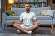 © Ivan - Fitness, meditation and healthy lifestyle concept - african american man meditating in lotus pose on exercise mat at home