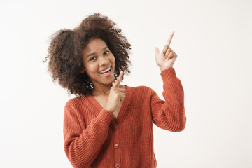 Portrait of African American young woman in red knitted sweater posing with smiling happiness face expression and point finger up to above on white background.