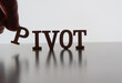 PIVOT spelled out with letters with hand placing the P, backlit by white on reflective surface. 