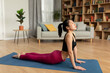 Fit korean lady doing yoga cobra pose or pilates, working out on mat in living room interior, copy space