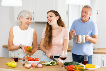 Wall Mural - Happy smiling parents enjoy weekend cook with adult daughter in kitchen